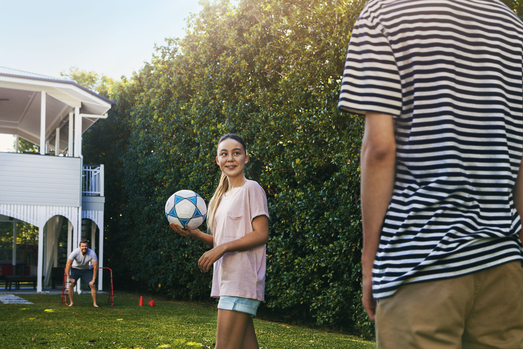 A girl holding a soccer ball in a backyard smiling at her brother